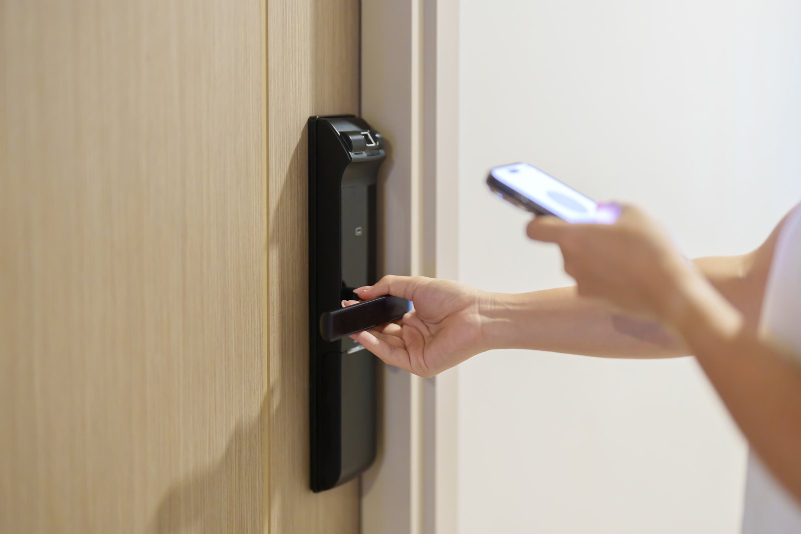 A hand using a smart lock keypad next to a phone