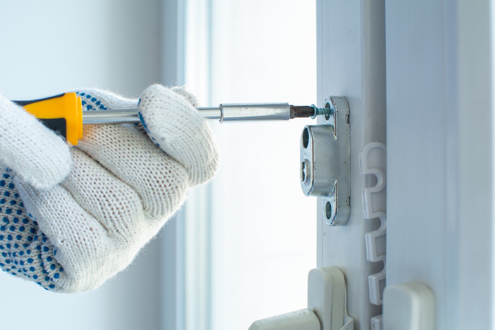 A gloved hand using a screwdriver to fit a multipoint lock keep to a uPVC door frame