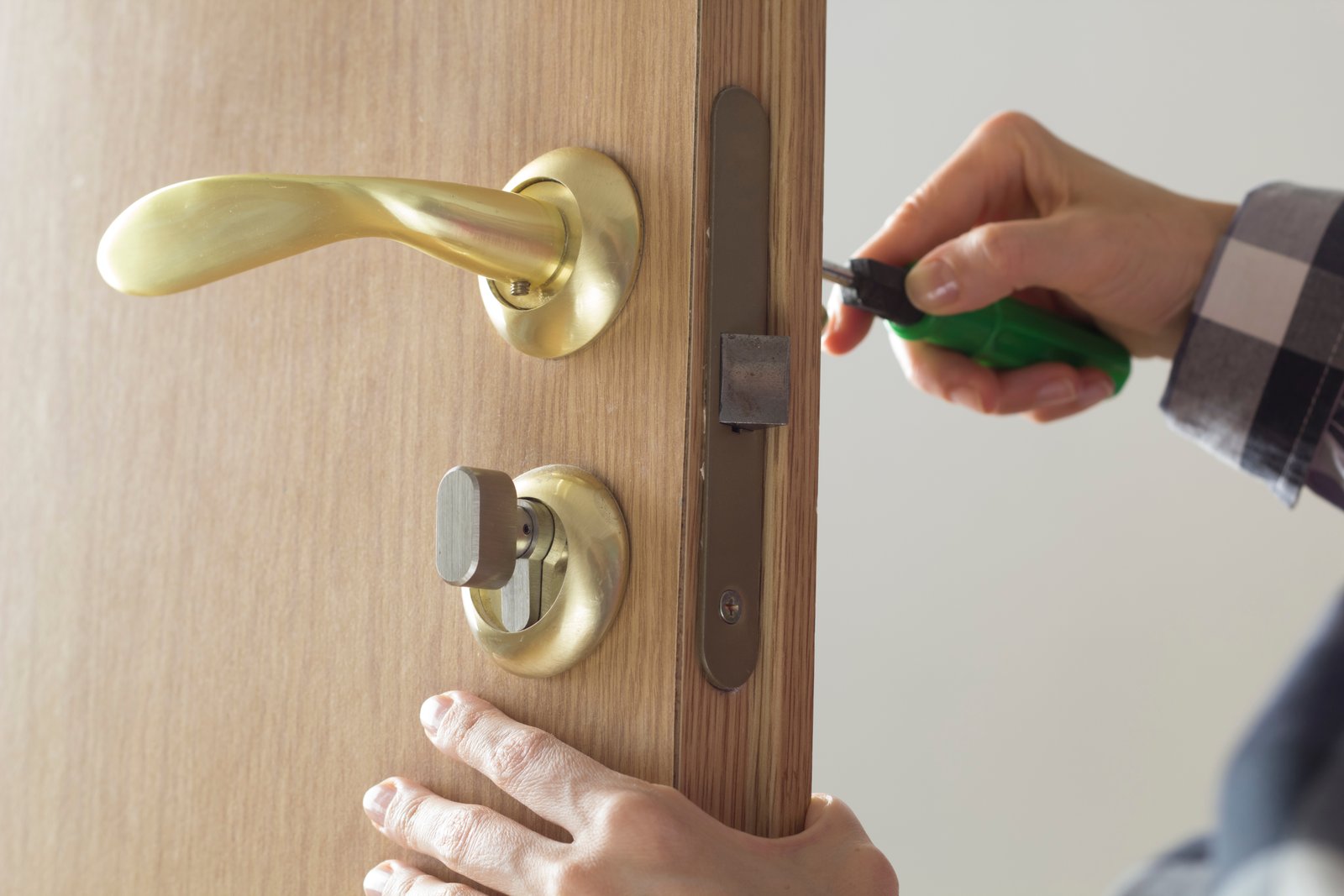 A hand using a screwdriver to fit a lock mechanism into a wooden door edge