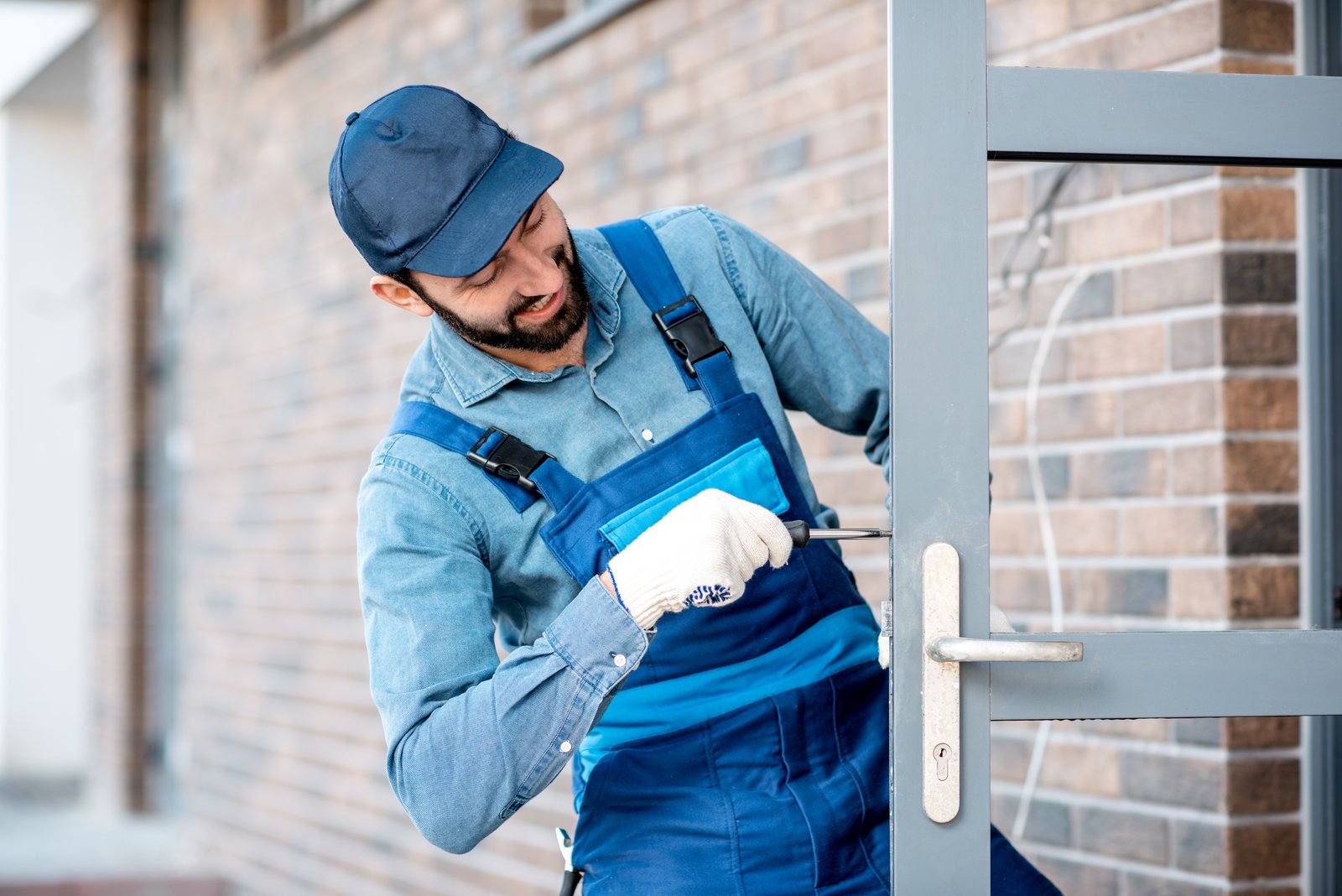 A tradesperson in workwear fitting a lock to a commercial glazed metal door