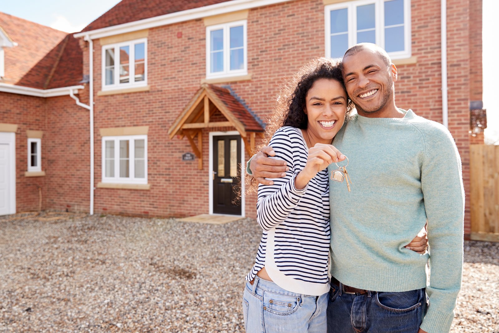 A smiling couple holding house keys outside a newly built brick home