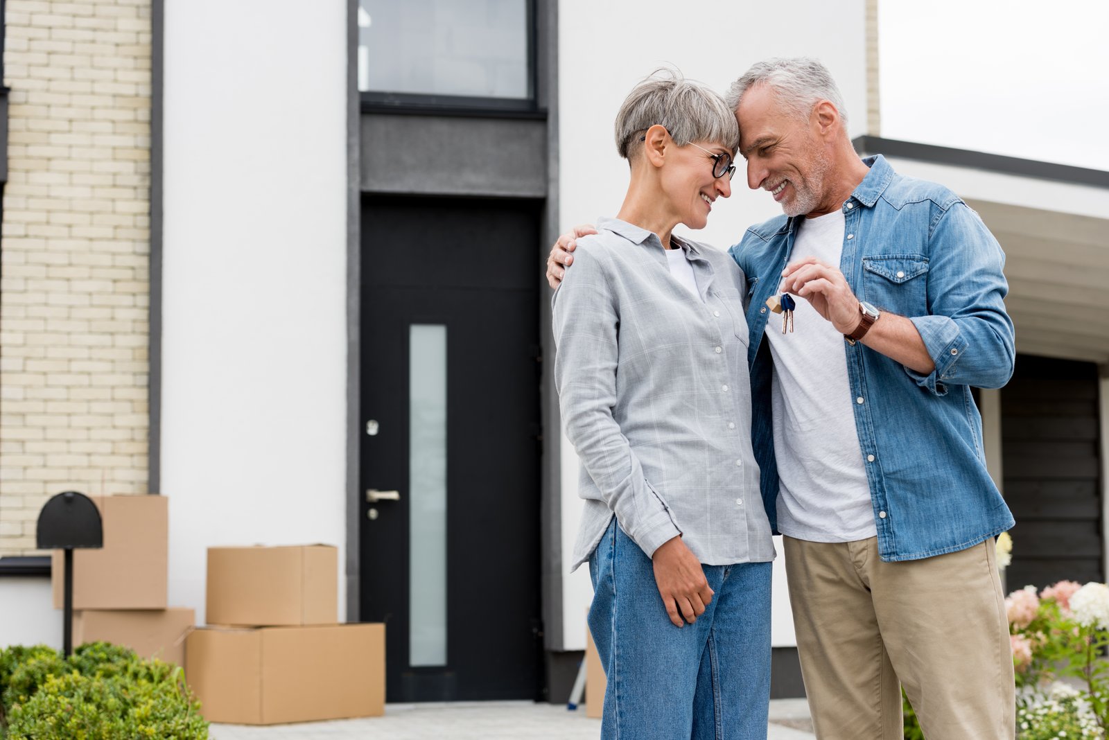 A couple holding keys with moving boxes outside their new home