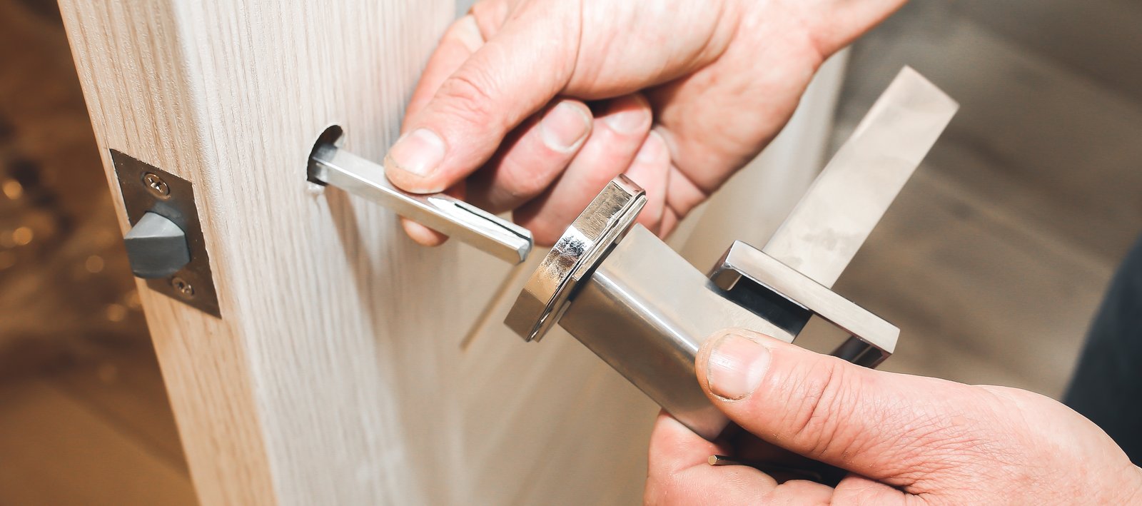 A hand using a drill to fit a lock mechanism into a white door frame with visible insulation