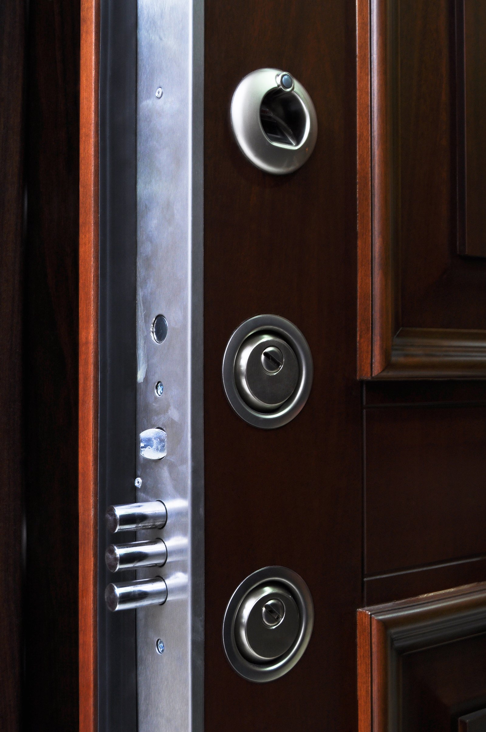 A close-up of a multipoint security deadbolt and peephole fitted to a wooden door
