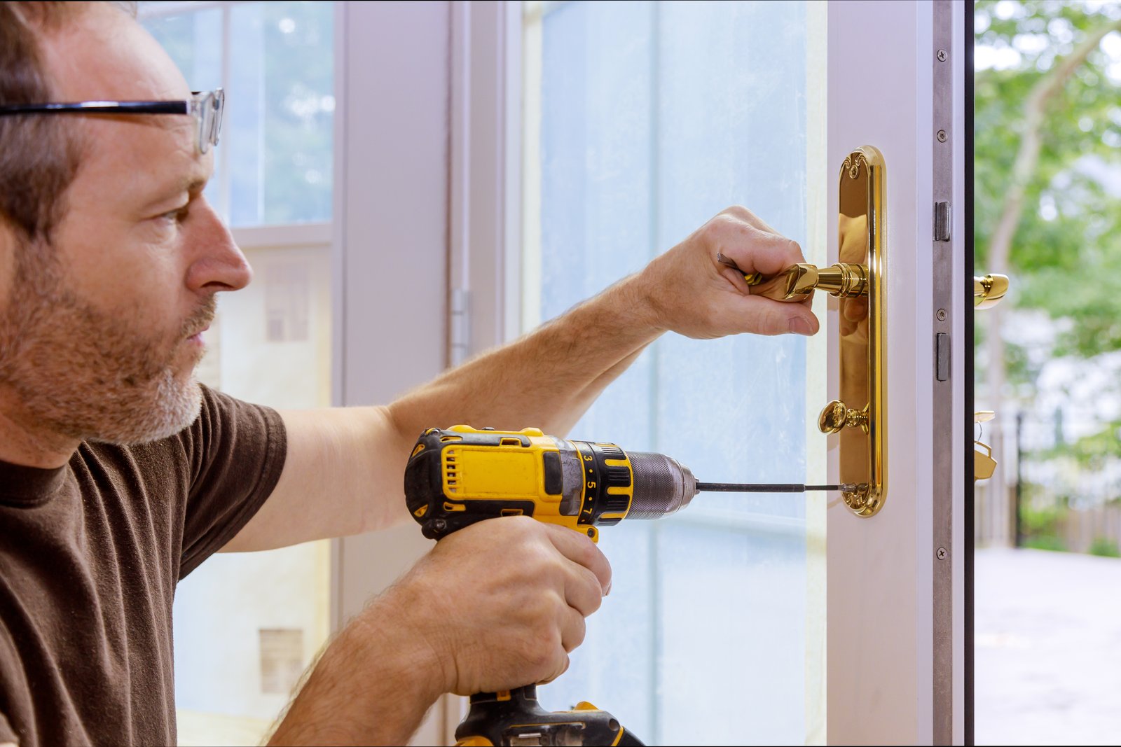 A man wearing glasses fitting a brass mortice lock into an exterior wooden door