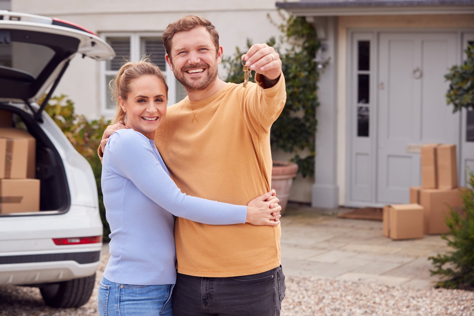 A couple with moving boxes and a car outside a house, holding keys