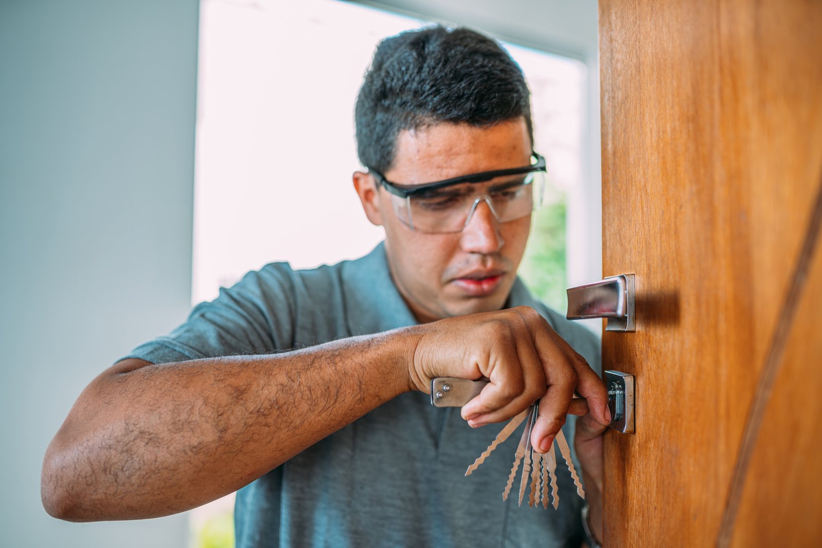 A locksmith wearing safety glasses working on a residential wooden door lock with hand tools