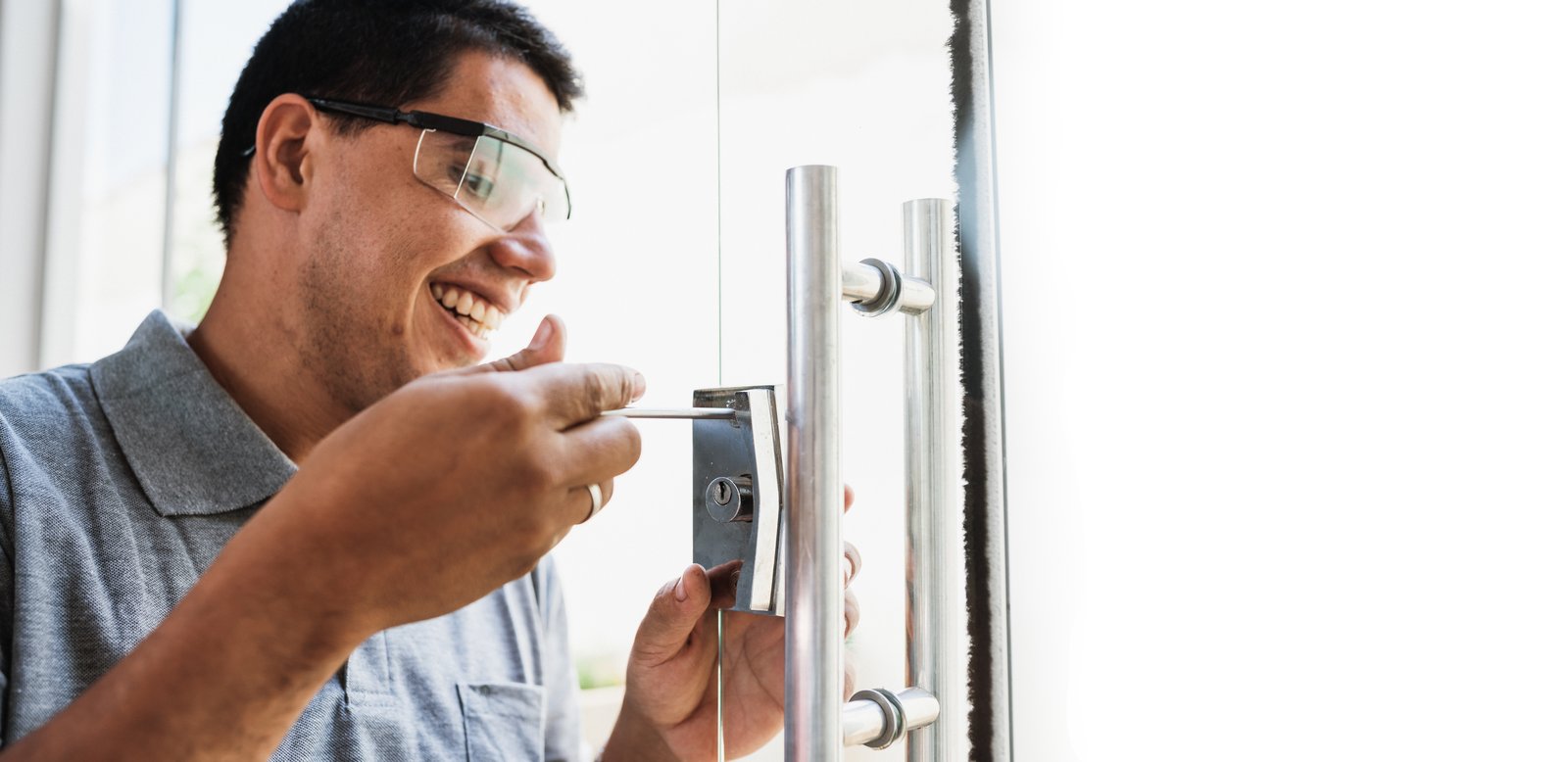 A smiling tradesperson fitting a lock into a glass-panelled commercial door