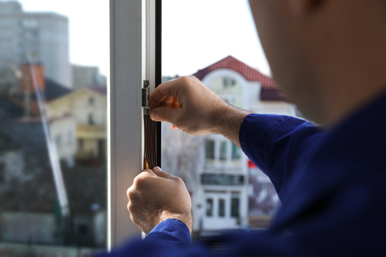 A tradesperson adjusting a window hinge mechanism with an urban street backdrop