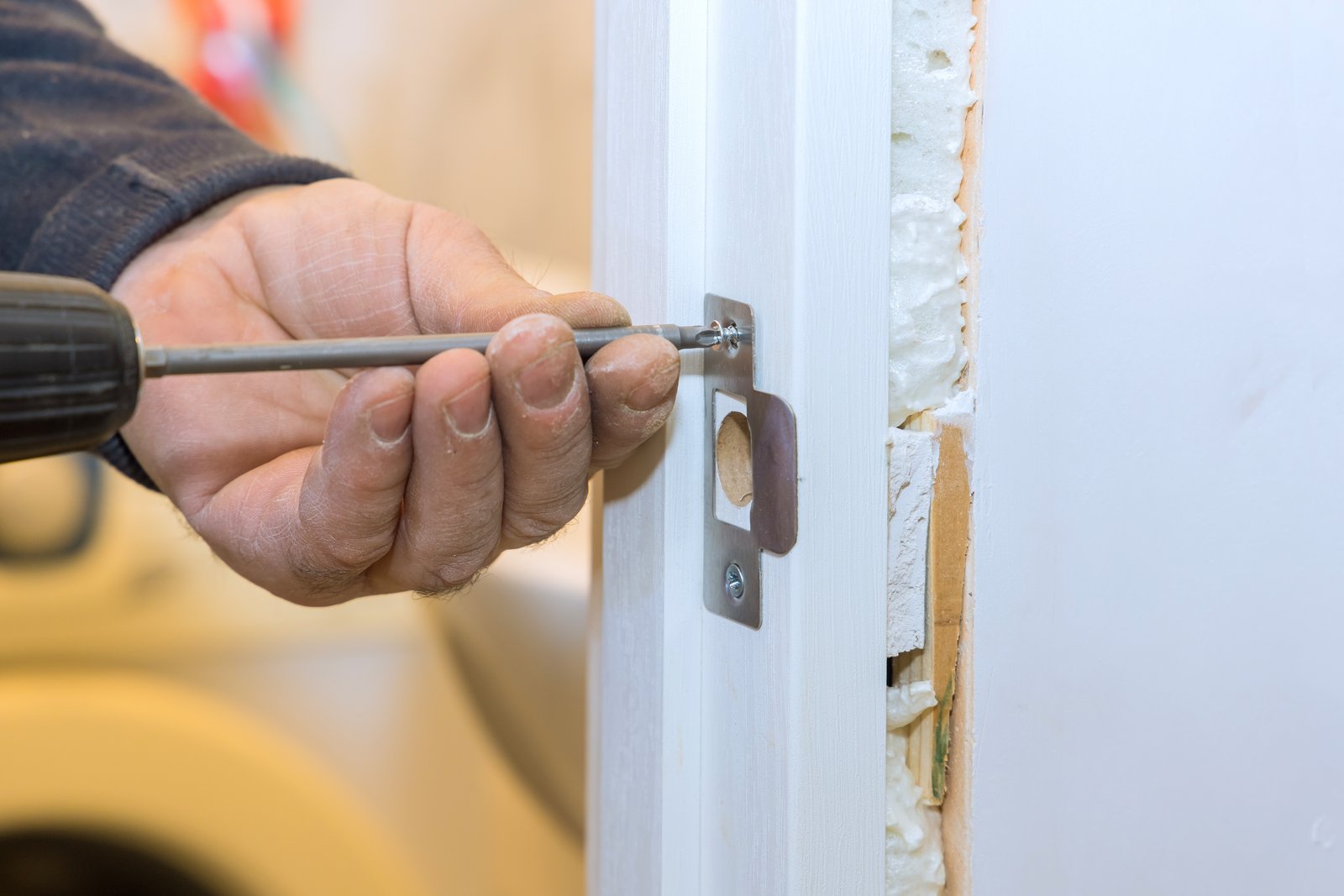 A hand fitting a mortice deadbolt into a newly hung door frame with visible insulation
