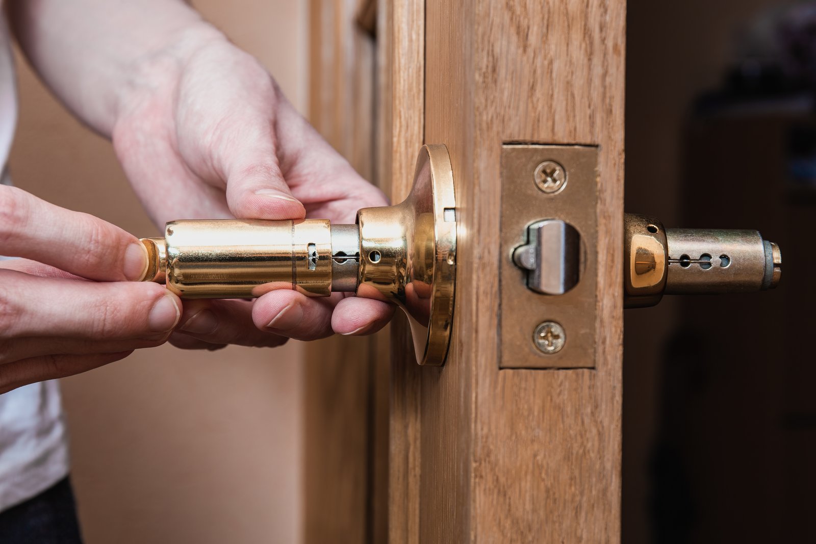 Hands installing a brass cylinder lock into a wooden door