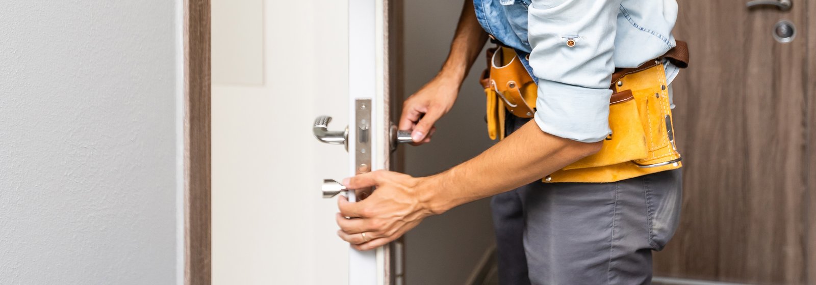A tradesperson with a tool belt opening a white panelled door