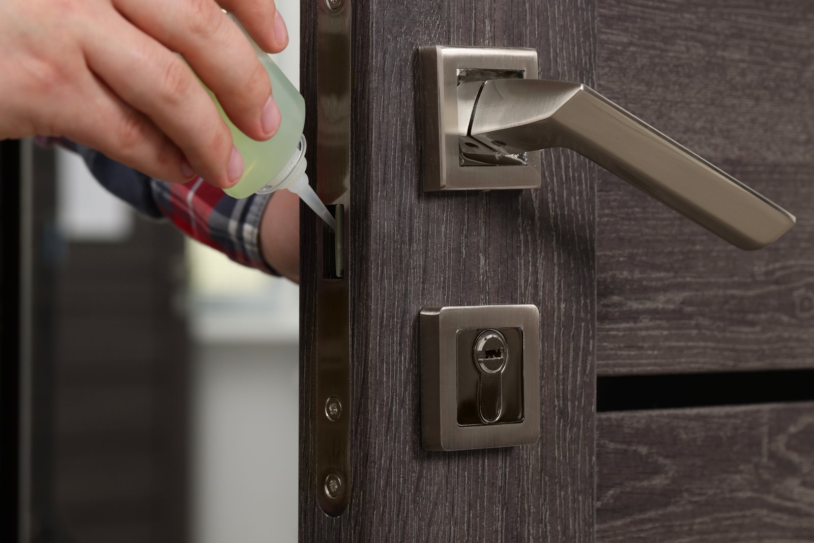 A hand applying lubricant to a door lock mechanism