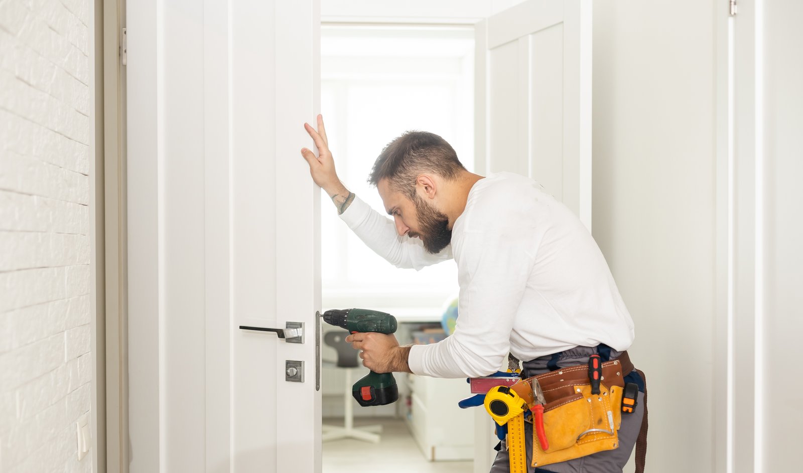 A tradesperson with a tool belt using a drill to fit an interior door lock