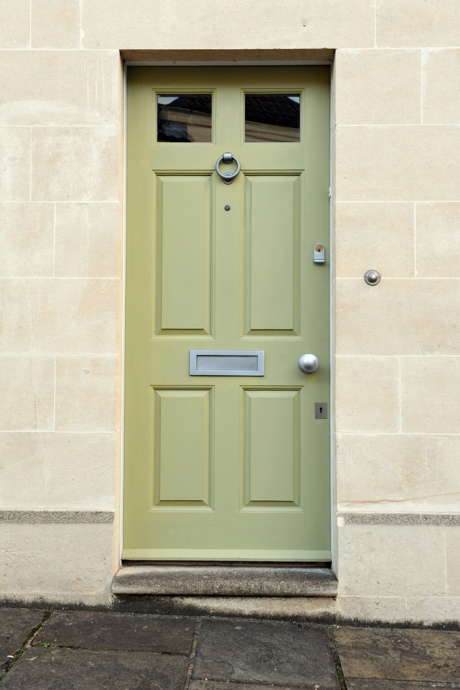 A period pale green panelled front door with a brass letterbox and door knocker on a stone townhouse
