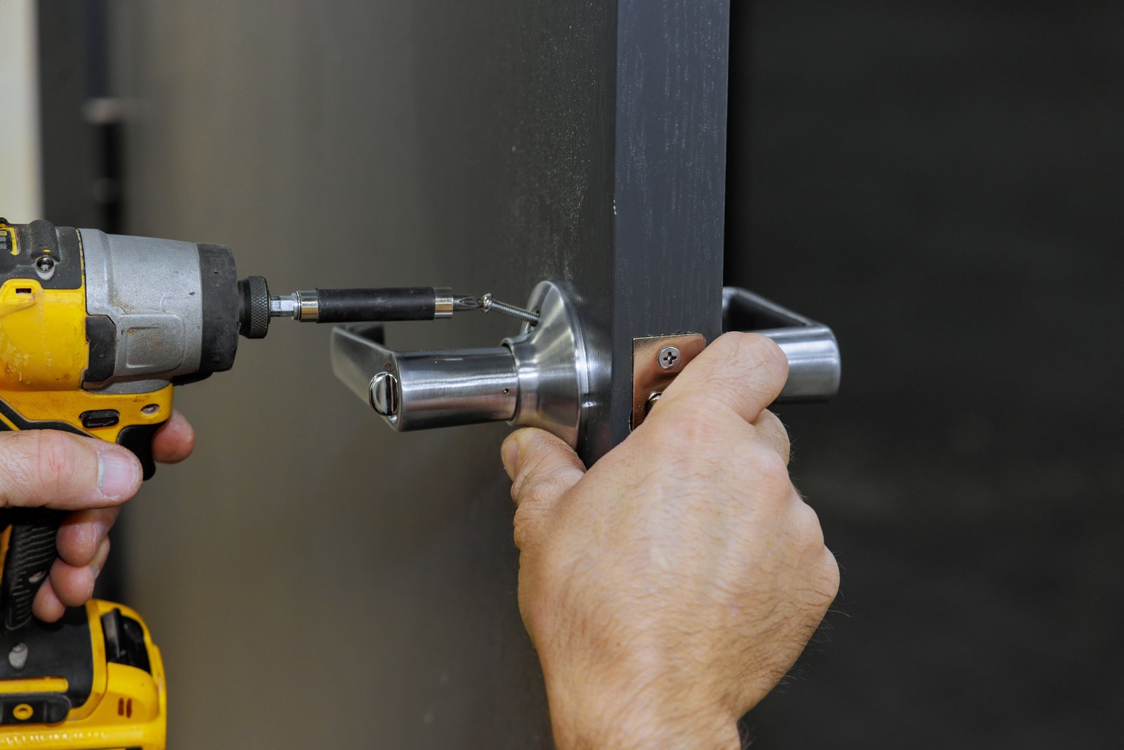 A hand using a drill to fit a lever handle mechanism into a dark door