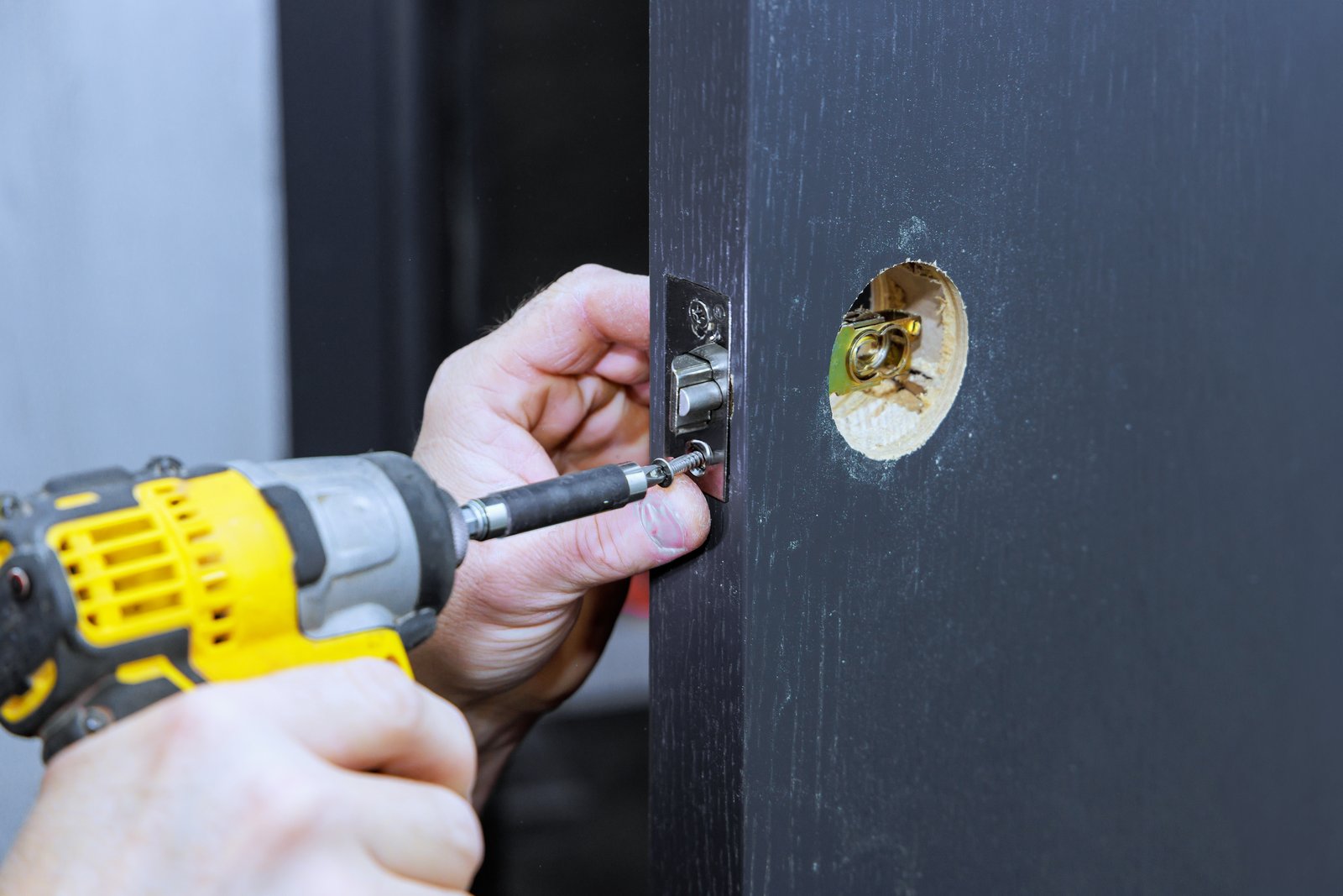 A hand using a drill to fit a new latch mechanism into a freshly bored door edge