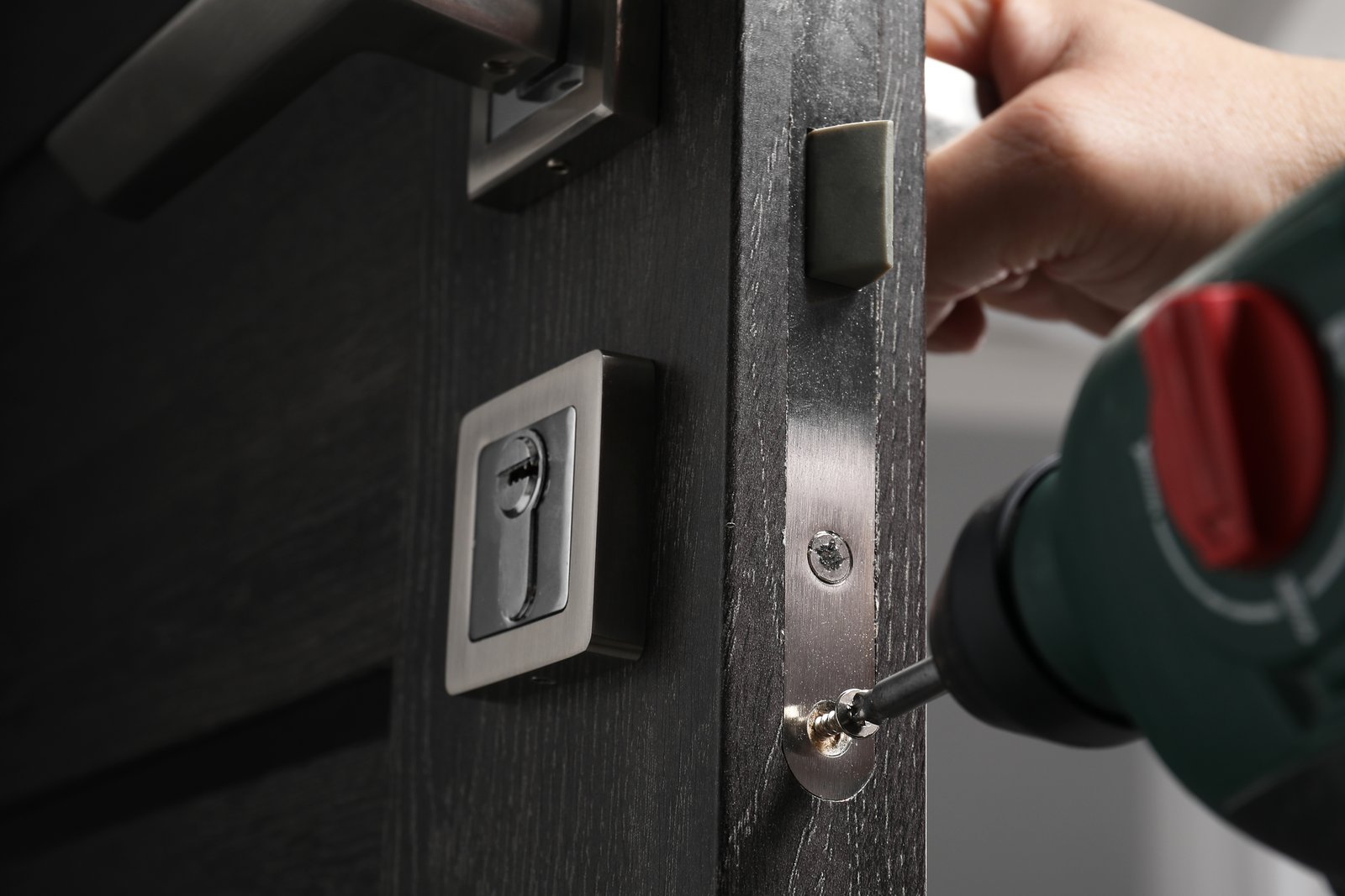 A hand fitting a modern strike plate mechanism into the edge of a dark door