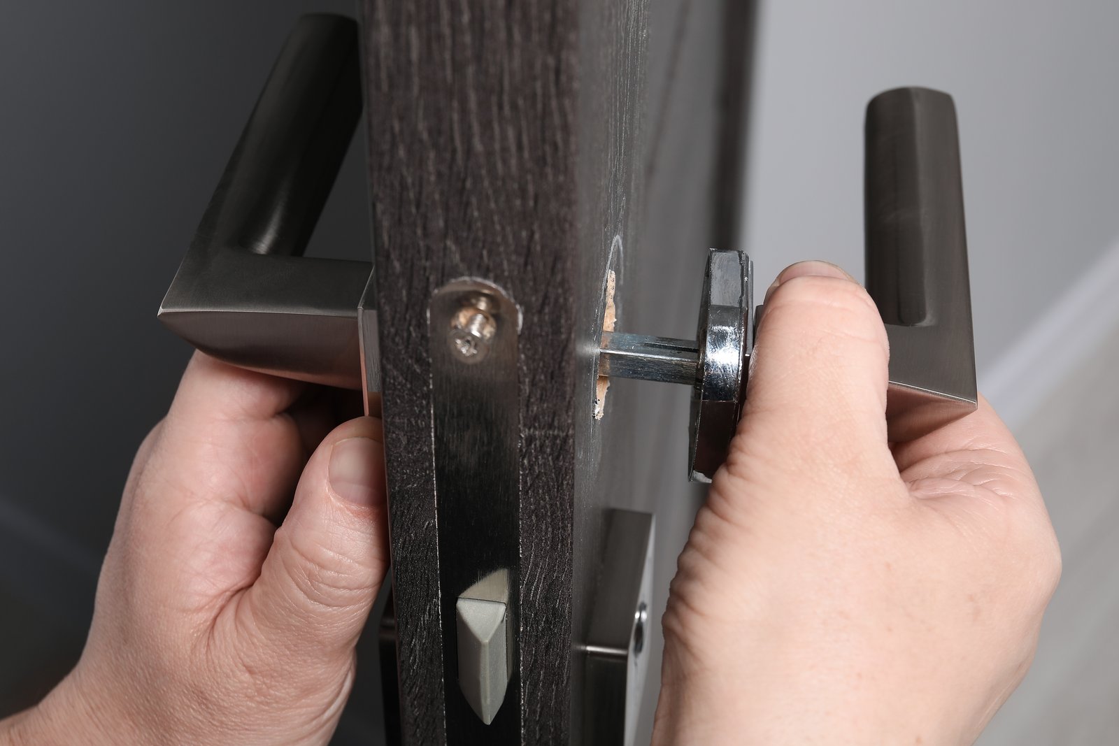 Two hands assembling a lever door handle set on a modern door