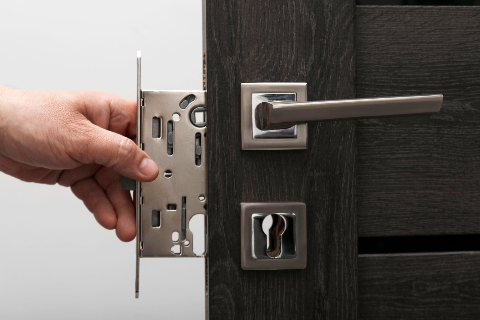 A hand fitting a modern multipoint lock mechanism to a commercial-grade door
