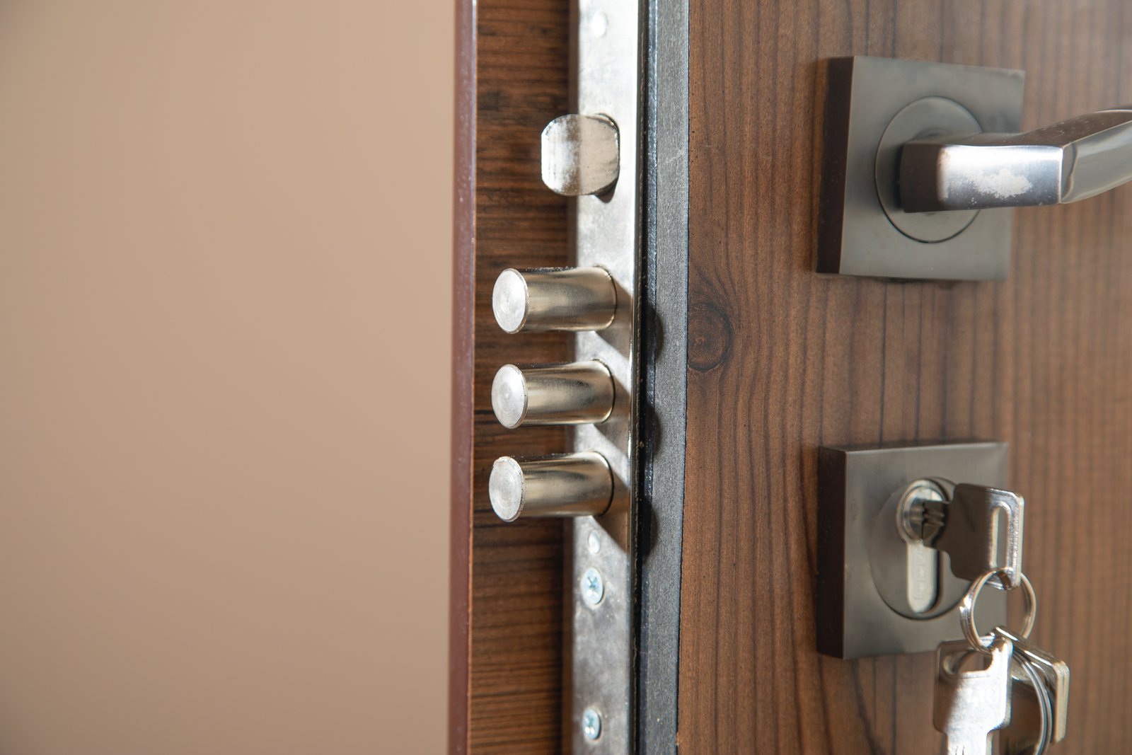 A close-up of a multipoint security deadbolt with keys in the cylinder on a wooden door