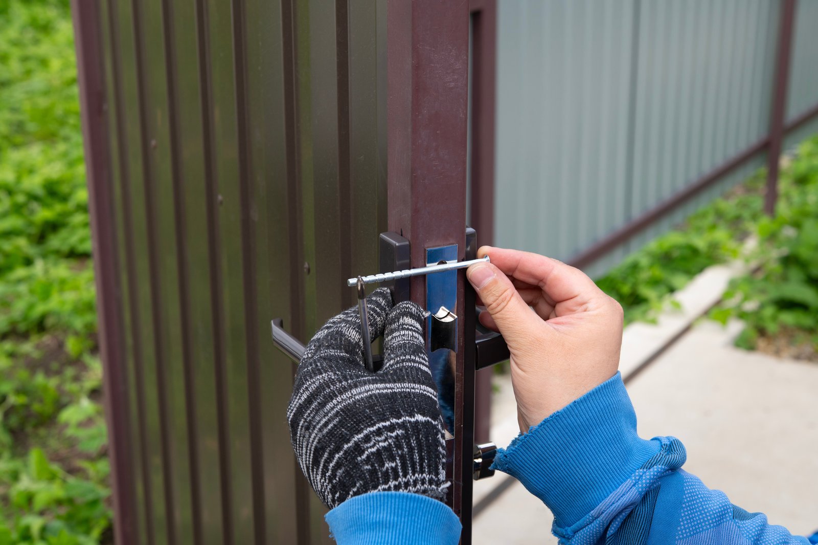A hand in a work glove fitting a bolt to a metal gate latch mechanism