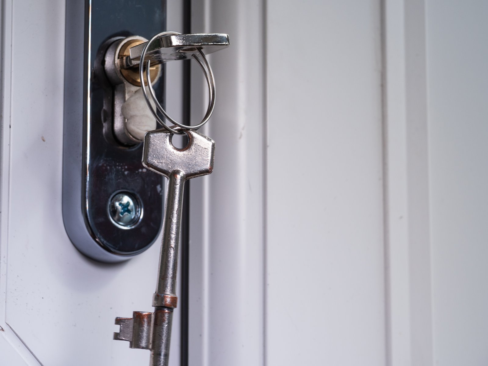 A traditional key hanging from a lock on a white uPVC door