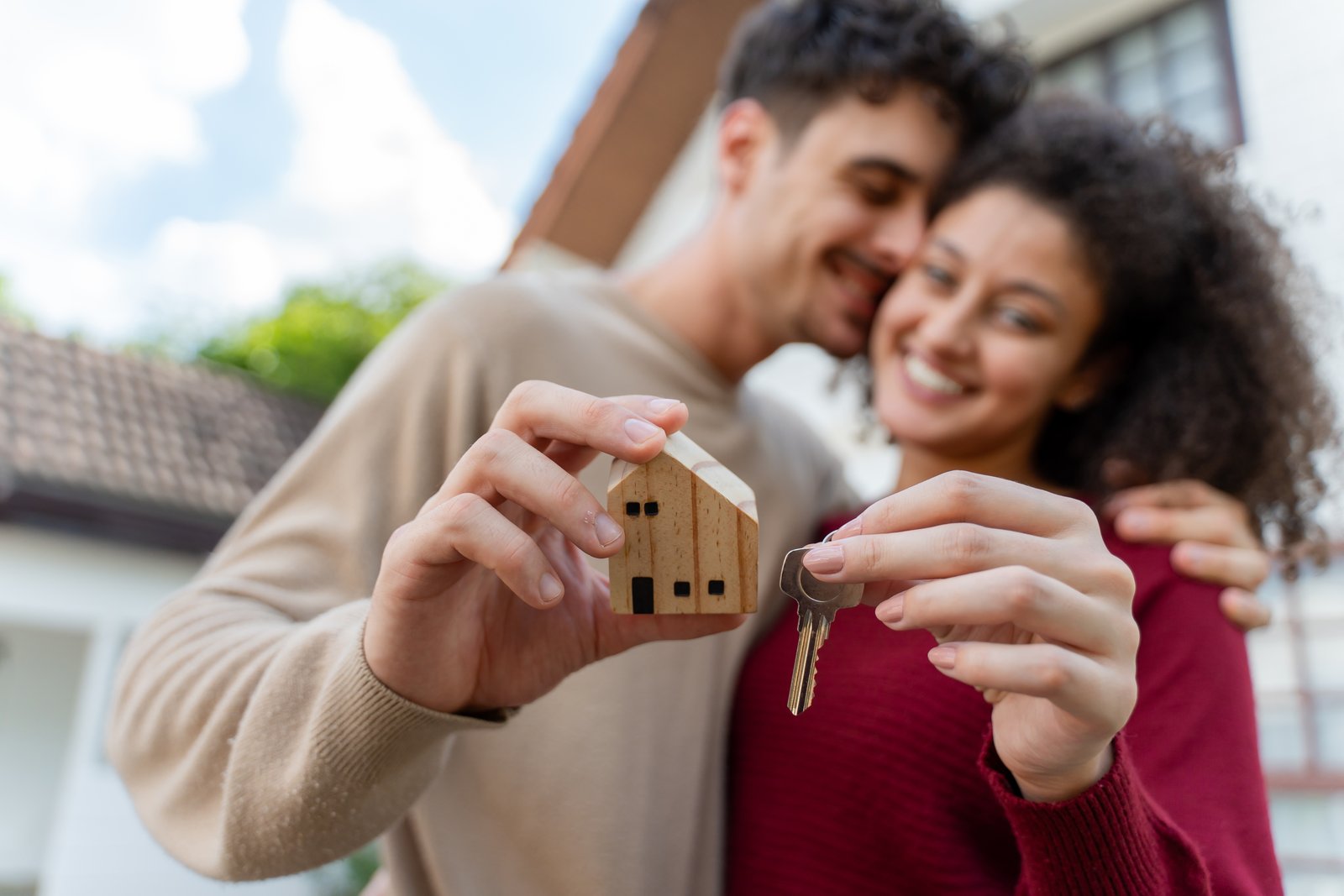 A smiling couple holding a small wooden house model and a key