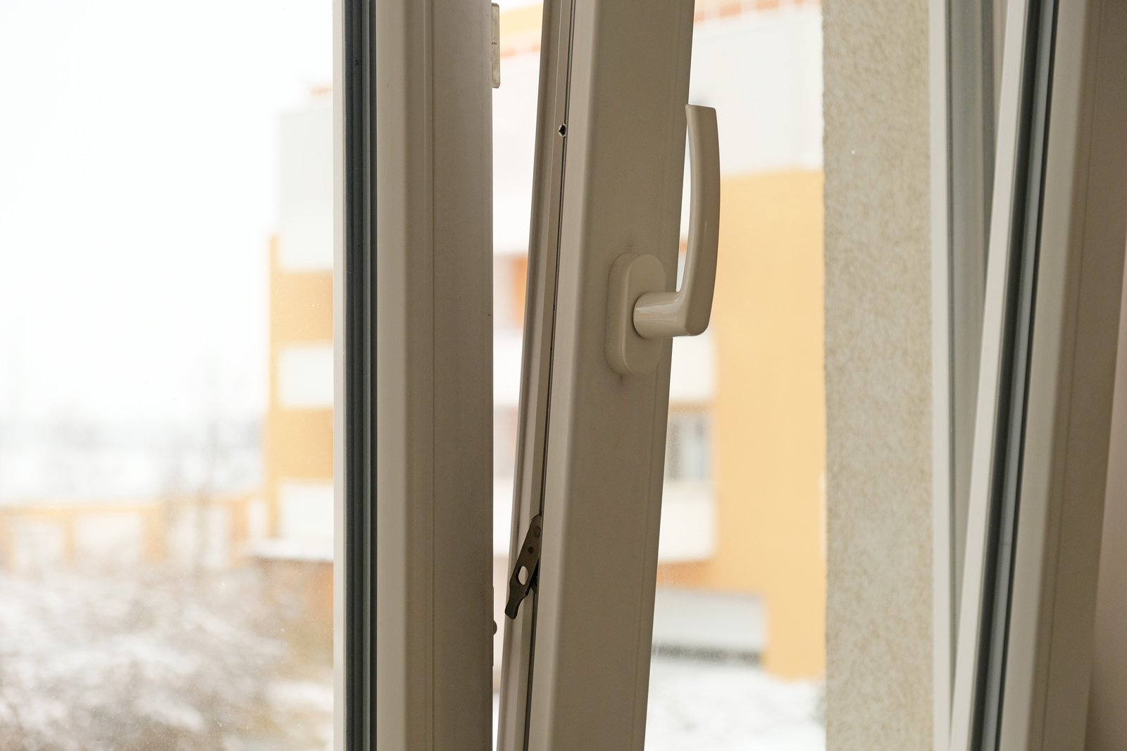 A hand adjusting a window handle mechanism with a snowy exterior visible beyond