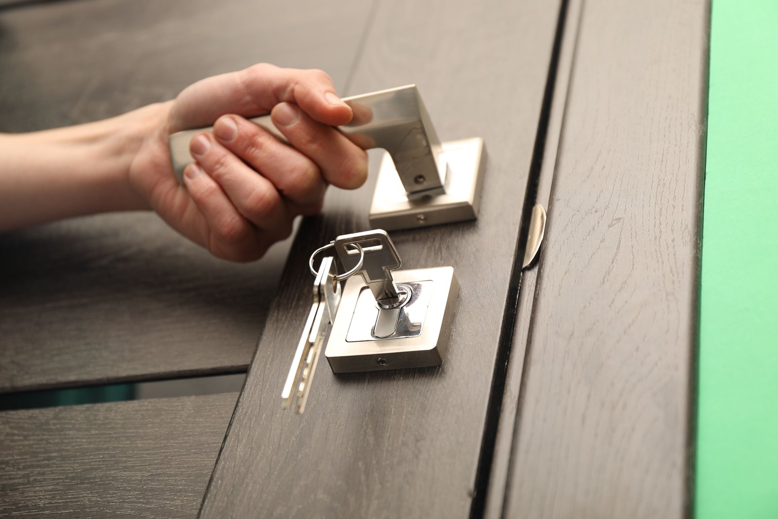 A hand opening a modern lever door handle with keys in the lock