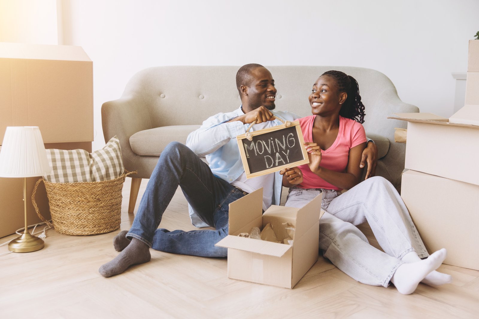 A couple sitting amid moving boxes holding a chalkboard sign reading Moving Day