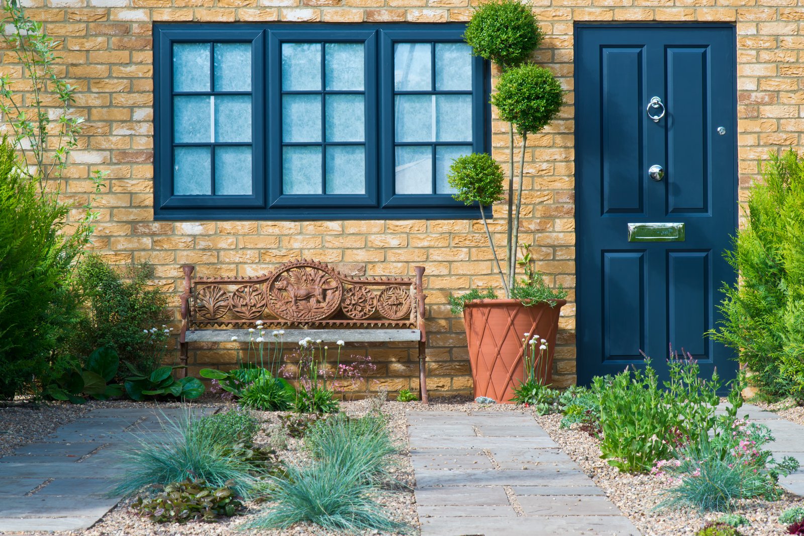 A navy front door with a brass letterbox and knocker on a brick house with a tidy front garden