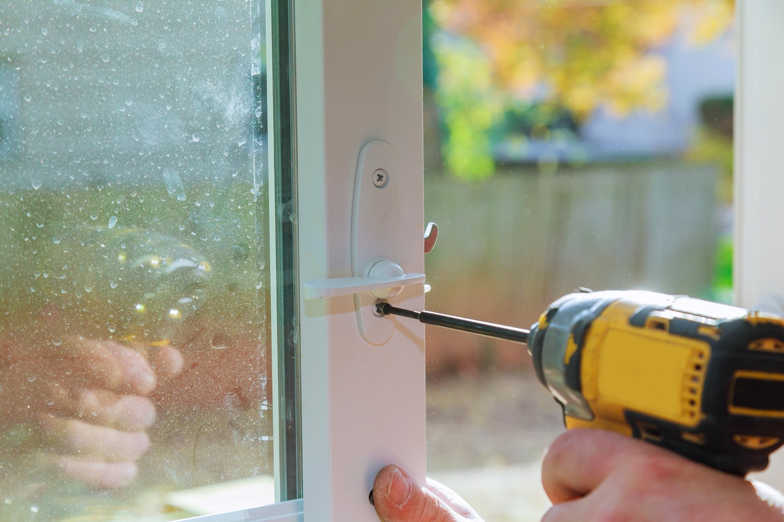 A tradesperson using a drill to fit a lock to a patio door outdoors