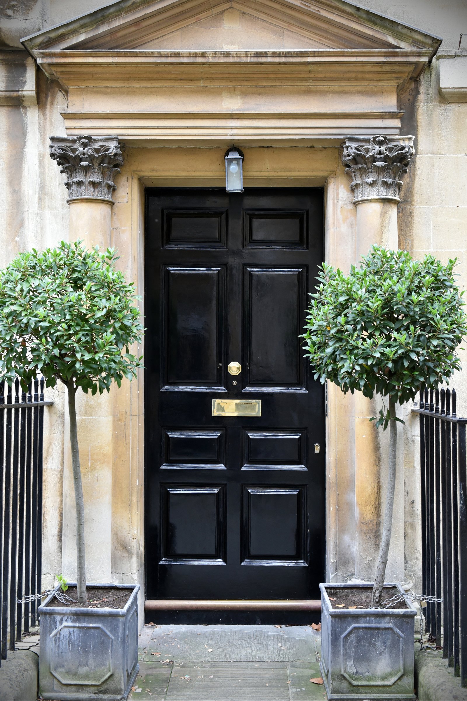 A grand black front door with a stone portico and topiary trees on a substantial period house